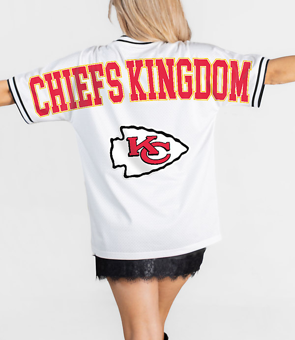 A person in a white "Chiefs Kingdom" jersey with the Kansas City Chiefs logo stands against a plain white background.