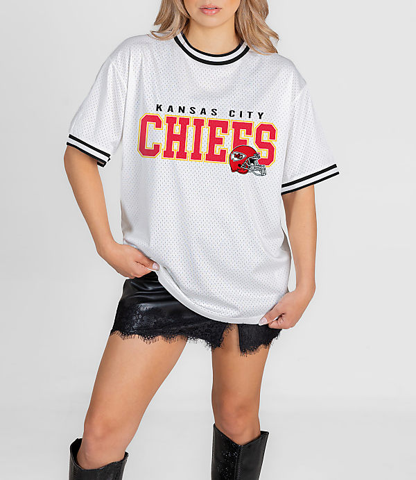 A woman in a white Kansas City Chiefs jersey and black skirt stands against a plain white background.