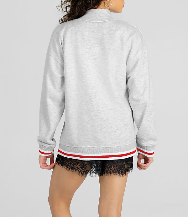 A woman in a grey sweatshirt and black lace shorts stands against a plain white background.