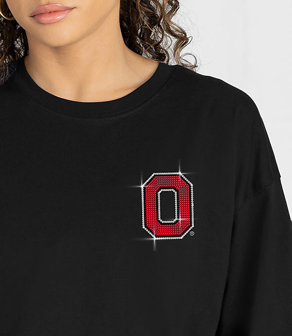 A woman wears a black t-shirt with a sparkling red and white "O" logo on the left chest, against a plain white background.