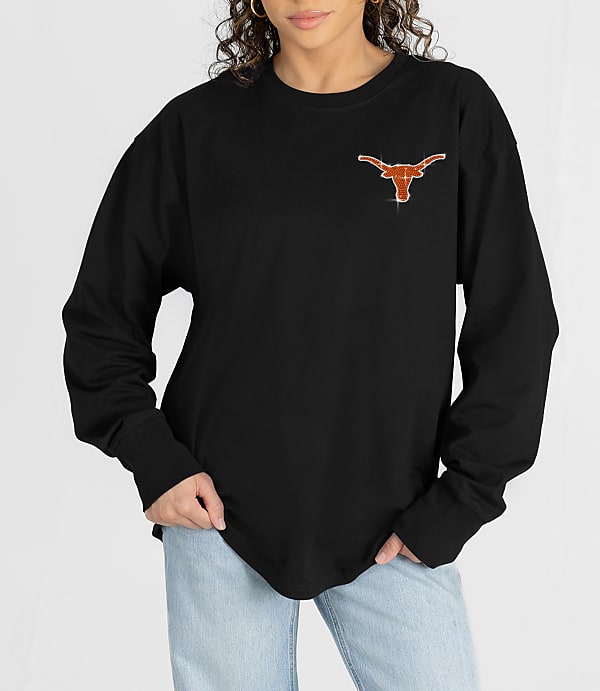 A person in a black long-sleeved shirt with a sparkly Texas Longhorns logo on the chest stands against a plain white background.