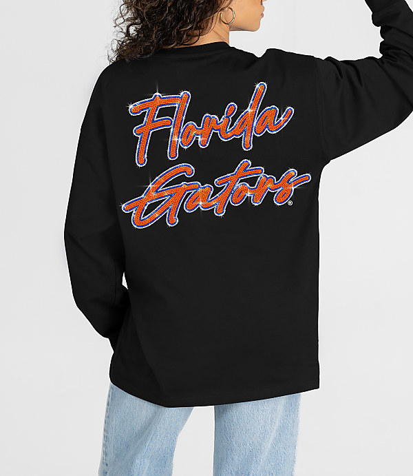 A person in a black long-sleeved shirt with "Florida Gators" written on the back stands against a plain white background.
