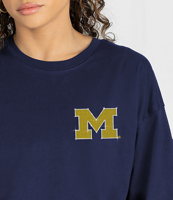 A woman in a navy blue shirt with a yellow and white "M" logo on the chest stands against a blurred white background.