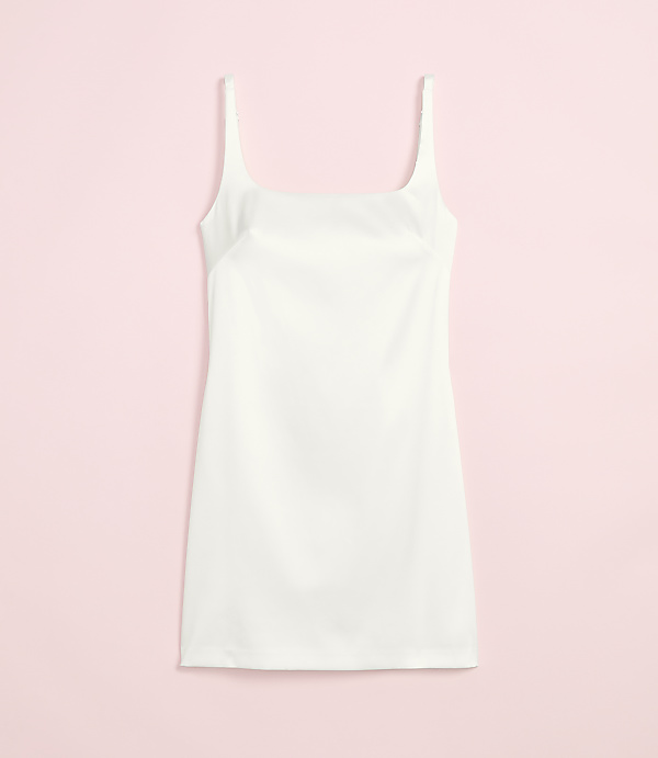 A white slip dress with thin straps is laid flat against a soft pink background.