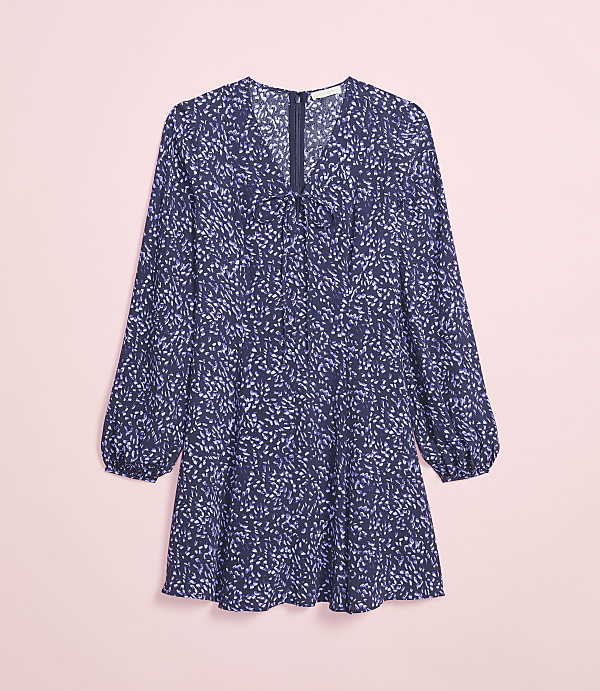 A long-sleeved navy blue dress with a scattered light purple floral print lies flat against a soft pink background.