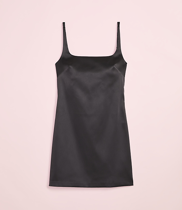 A black satin slip dress with thin straps is centered against a soft pink background.
