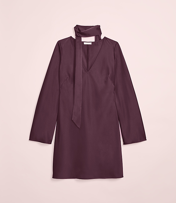 A plum-colored dress with a tie neck is laid flat against a soft pink background.