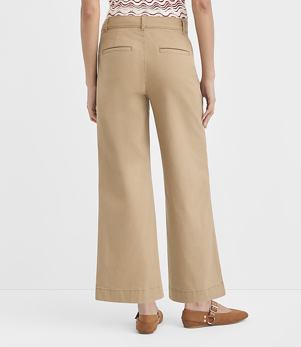 A person wearing tan cropped wide-leg pants and brown flats stands against a plain white background.