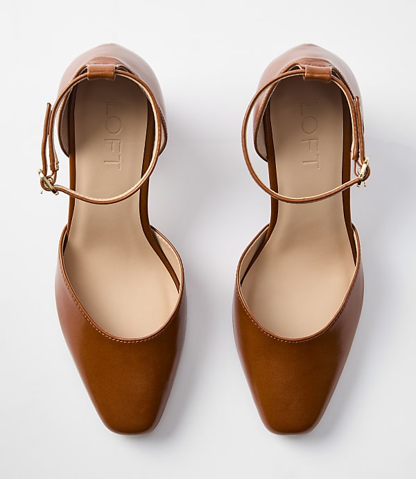 A pair of brown leather t-strap heels with a white background.
