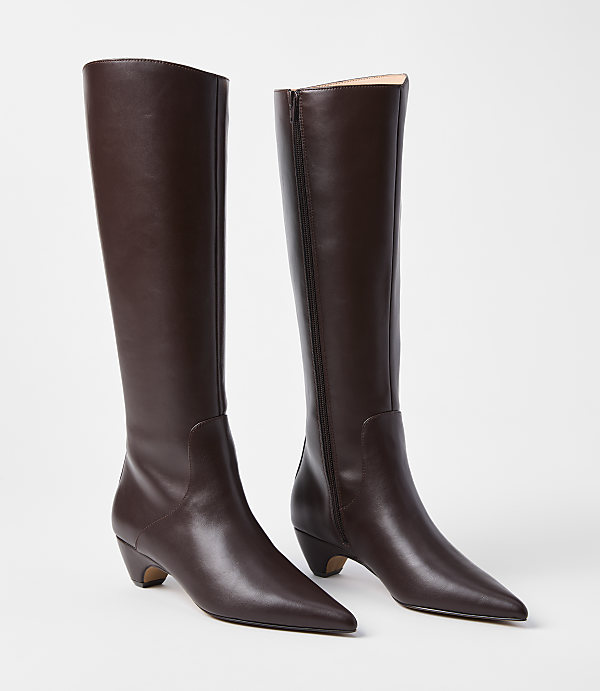A pair of dark brown leather knee-high boots with pointed toes and low heels stand on a plain white background.