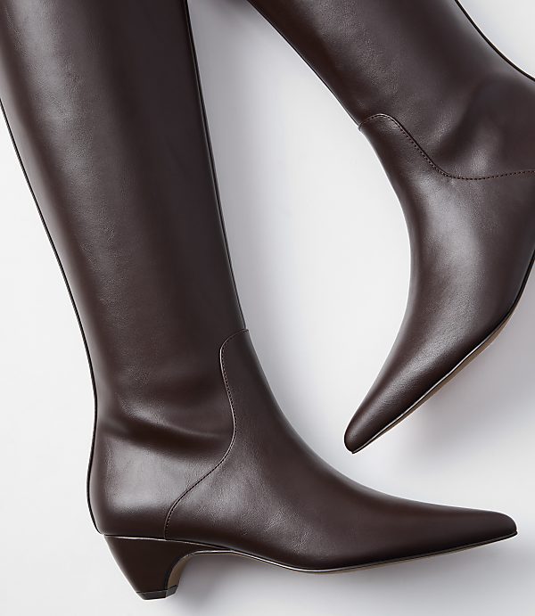 A pair of dark brown leather knee-high boots with pointed toes and low heels are displayed against a plain white background.