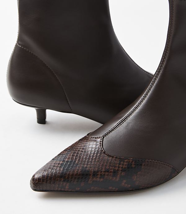 A close-up of dark brown pointed-toe boots with a snakeskin accent on the toe, set against a plain white background.