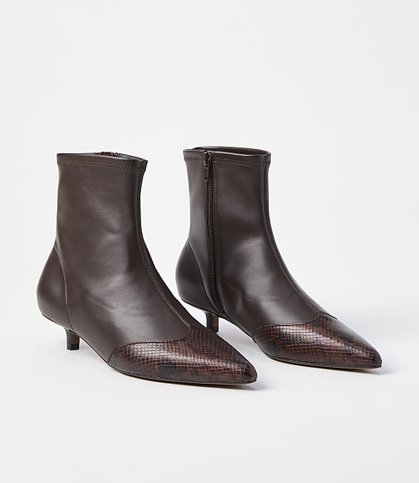 A pair of brown leather ankle boots with pointed, snakeskin-patterned toes and kitten heels stand on a white background.