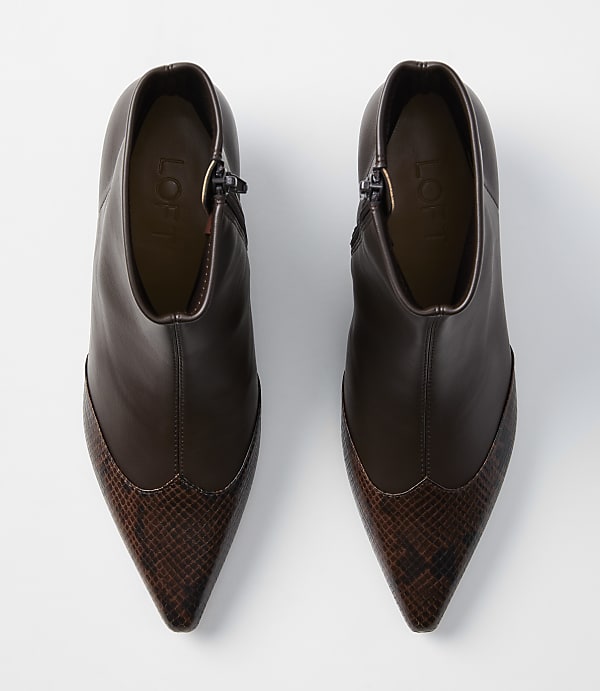 A pair of brown leather ankle boots with pointed snake-print toes are displayed against a plain white background.