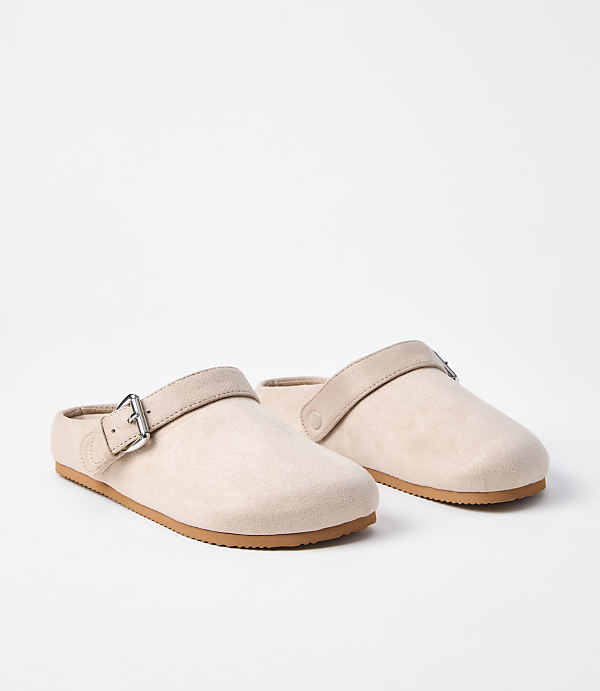 A pair of light pink clogs with tan straps and buckles rests on a white background.