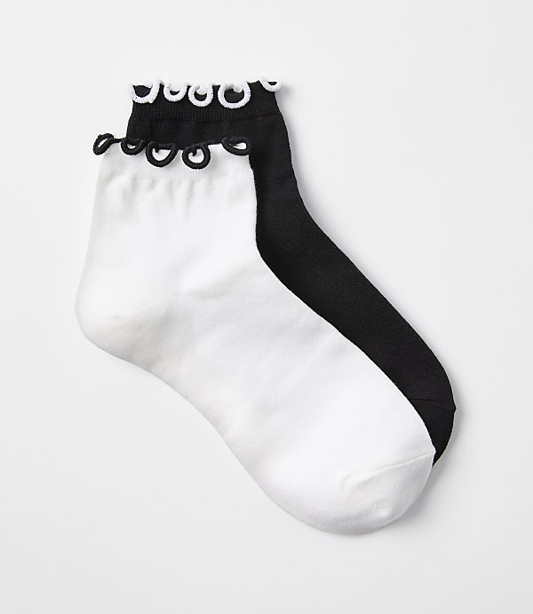 A pair of white and black ankle socks with ruffled cuffs are laid out on a plain white background.