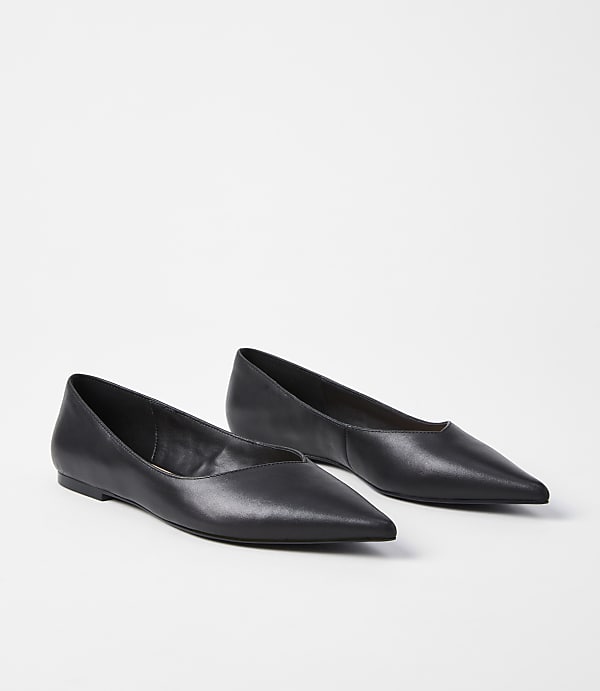 A pair of black pointed-toe flats rests on a plain white background.