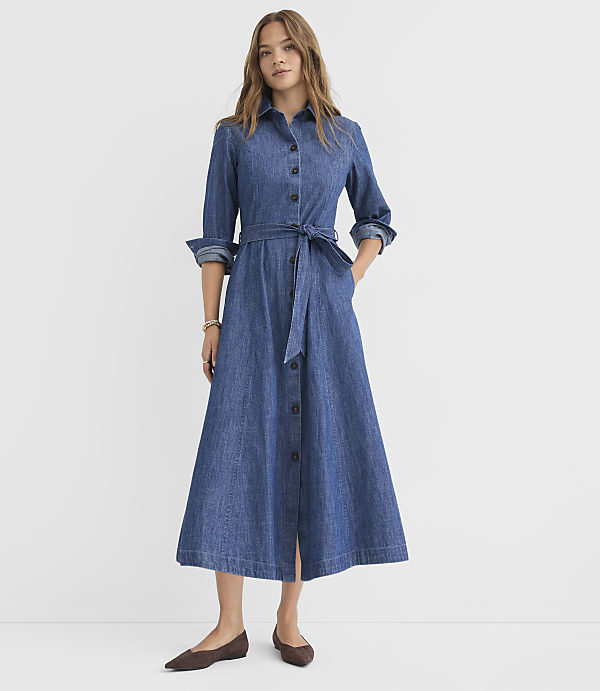 A woman in a denim shirt dress stands against a plain white background.