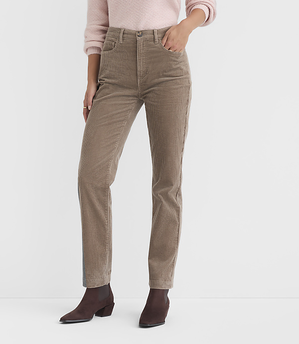 A person in a pink sweater and tan corduroy pants stands against a plain white background.