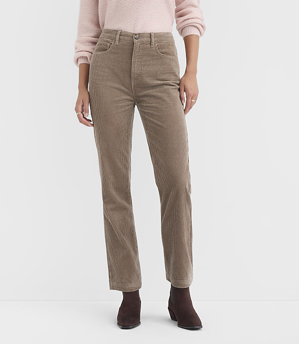 A person stands in the foreground wearing a pink sweater and tan corduroy pants, with a plain white background.