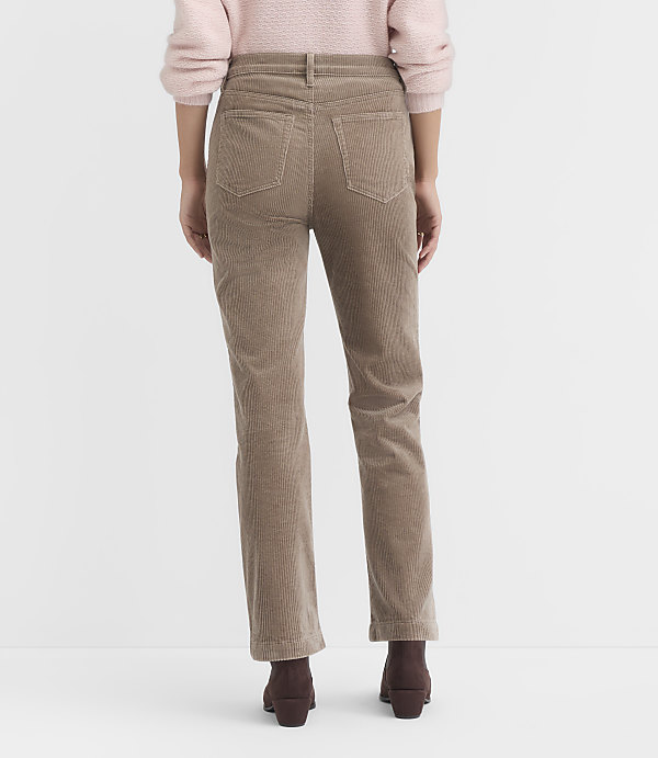 A person wearing tan corduroy pants and a pink sweater stands against a plain white background.