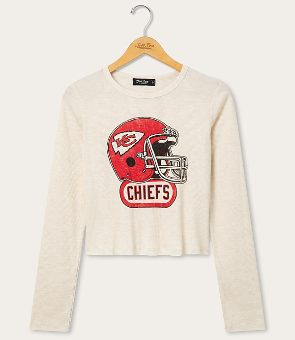 A cream-colored long-sleeved shirt with a distressed Kansas City Chiefs helmet graphic is displayed on a wooden hanger against a plain white background.