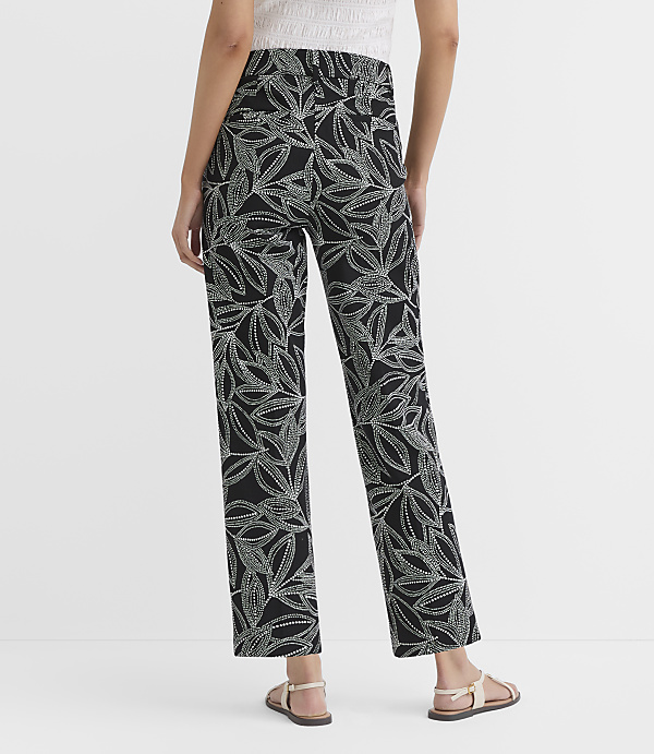 A person stands in the foreground wearing black pants with a white leaf pattern and sandals, against a plain white background.