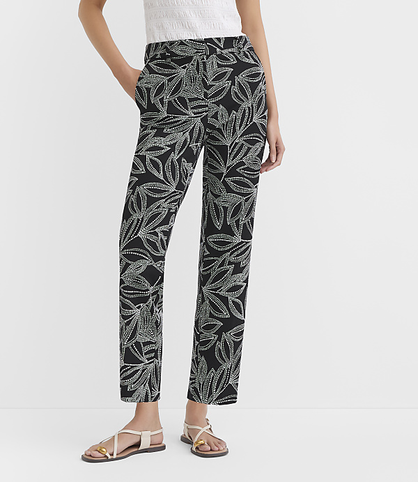 A person models black pants with a white leaf pattern, standing against a plain white background.