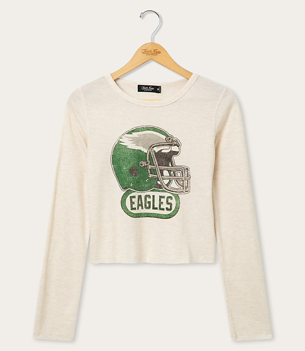 A cream-colored long-sleeved shirt with a distressed graphic of a green football helmet and the word "EAGLES" hangs on a wooden hanger against a plain white background.