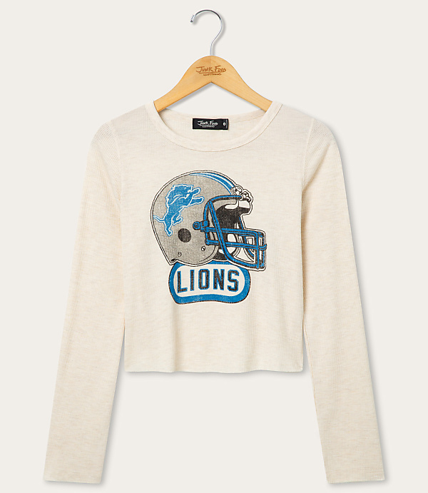 A cream-colored long-sleeved shirt with a distressed Detroit Lions helmet graphic is displayed on a hanger against a plain white background.
