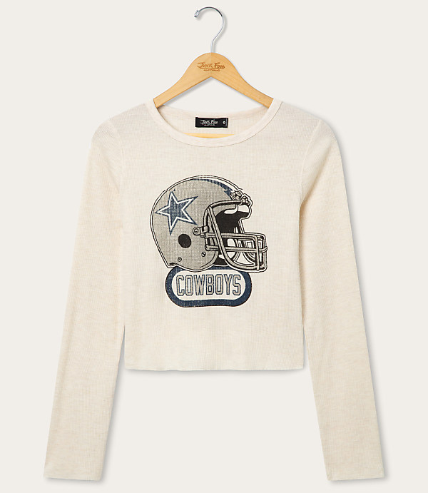A cream-colored long-sleeved shirt with a graphic of a Dallas Cowboys helmet is displayed on a hanger against a plain white background.