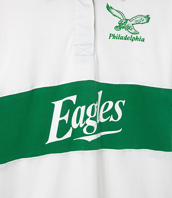 A white rugby shirt with a green stripe across the chest displays "Eagles" in large white lettering, while a green eagle logo and "Philadelphia" are embroidered on the upper right chest.