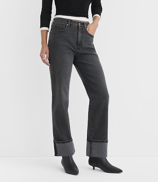 A person in dark wash cuffed jeans and black boots stands against a plain white background.