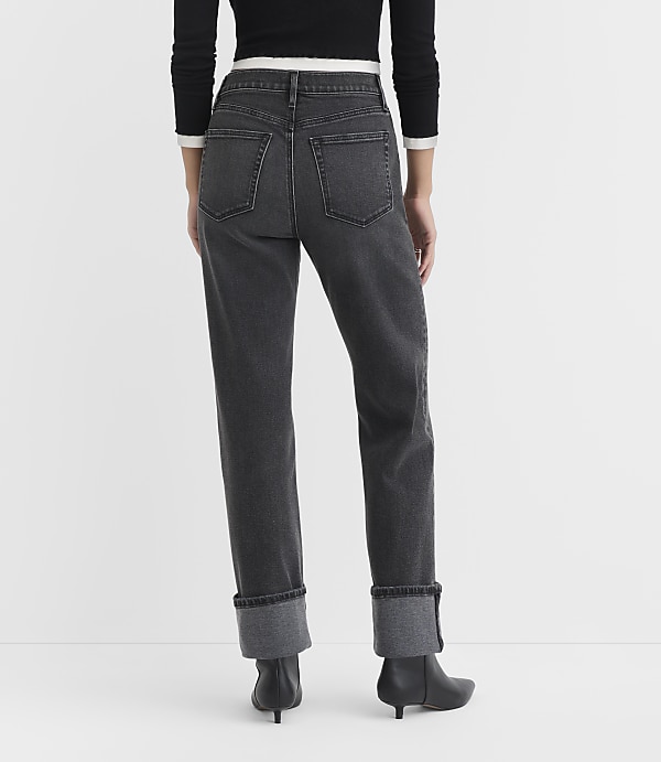 A person wearing dark wash cuffed jeans and black heeled boots stands against a plain white background.