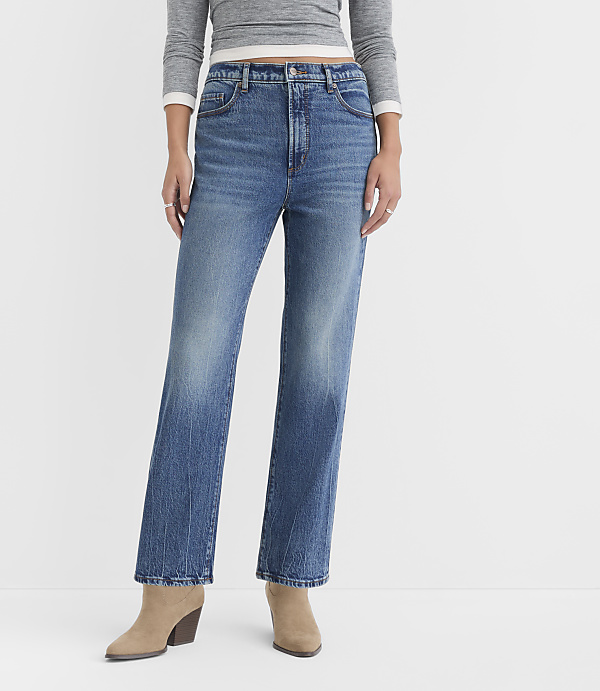 A person wearing high-waisted, straight-leg blue jeans and tan ankle boots stands against a plain white background.