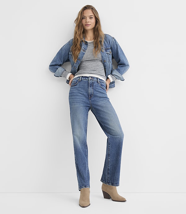 A woman in a denim jacket and jeans stands against a plain white background.