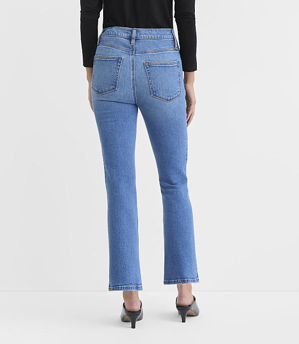 A person wearing blue jeans and black heels stands against a plain white background.