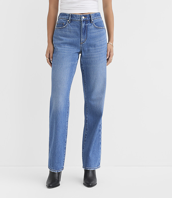 A person wearing blue jeans and black boots stands against a plain white background.