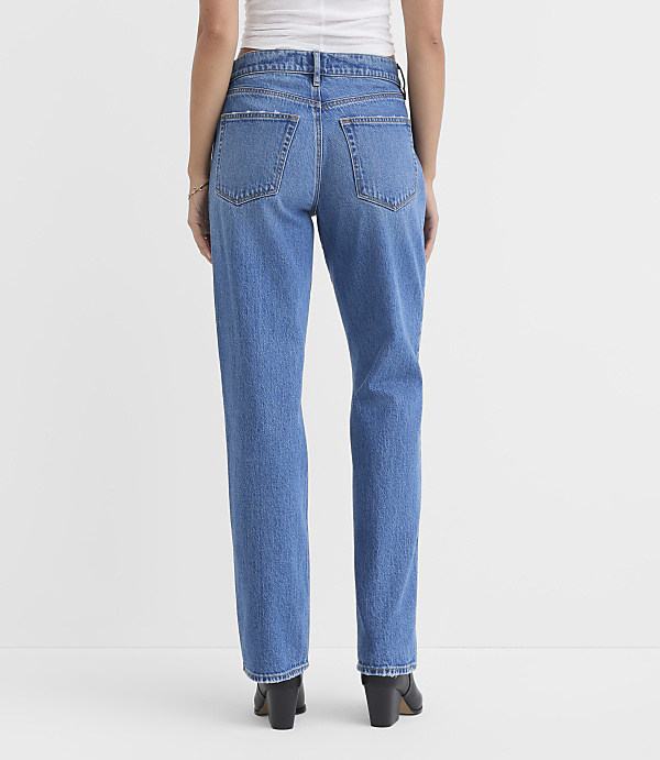 A person wearing blue jeans and black boots stands against a plain white background.