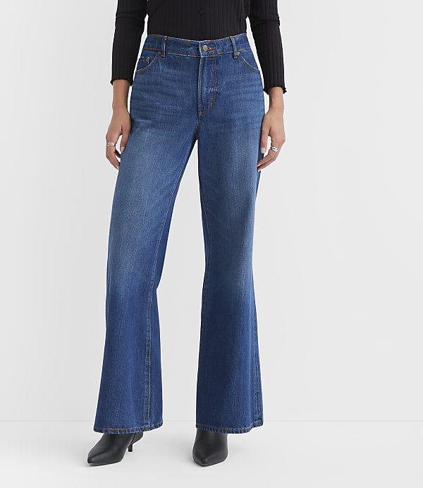 A person wearing flared blue jeans and black heeled boots stands against a plain white background.