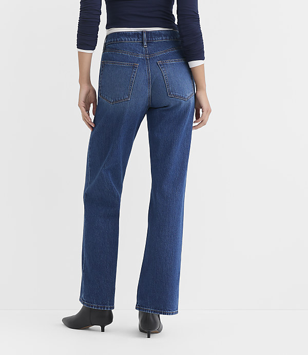 A person wearing dark blue jeans and black heeled boots stands against a plain white background.
