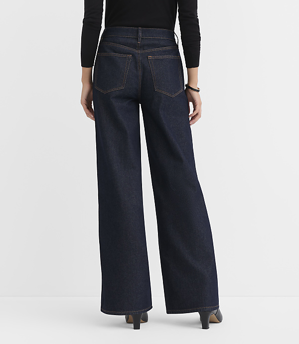 A person wearing dark wash wide-leg jeans and black heels stands against a plain white background.
