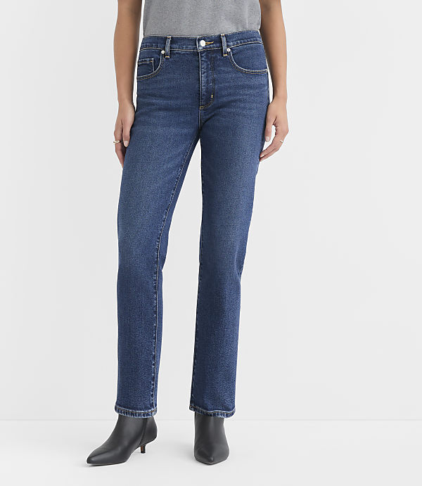 A person stands in dark wash straight-leg jeans and black ankle boots against a plain white background.