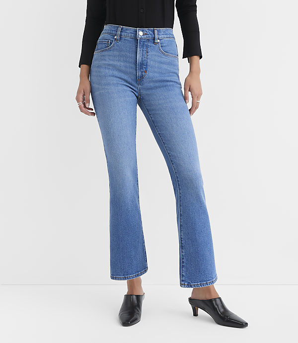 A person wearing light-wash flared jeans and black heeled mules stands against a plain white background.