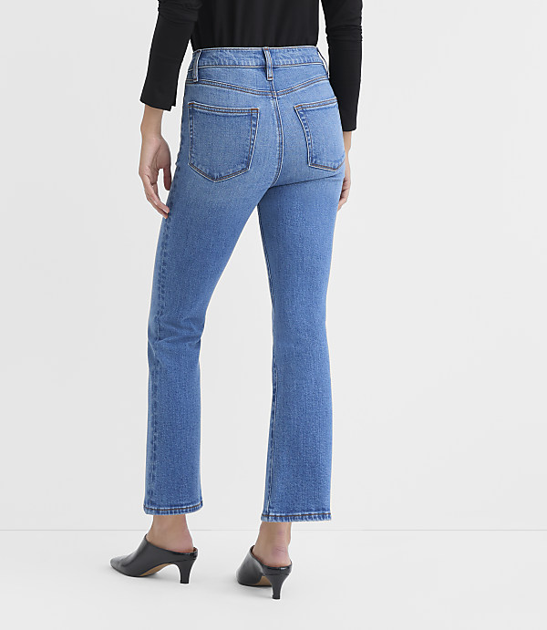 A person wearing blue jeans and black heels stands against a plain white background.