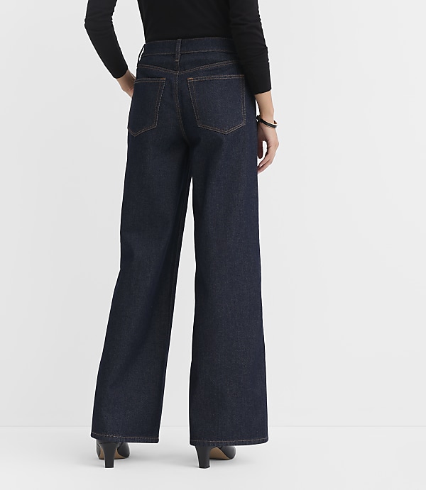 A person wearing dark wash wide-leg jeans and black heels stands against a plain white background.