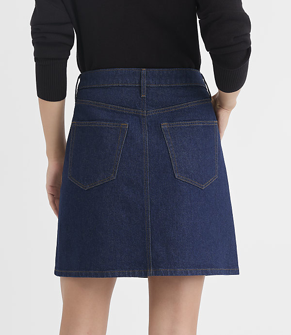 A person wearing a dark blue denim skirt stands against a plain white background.
