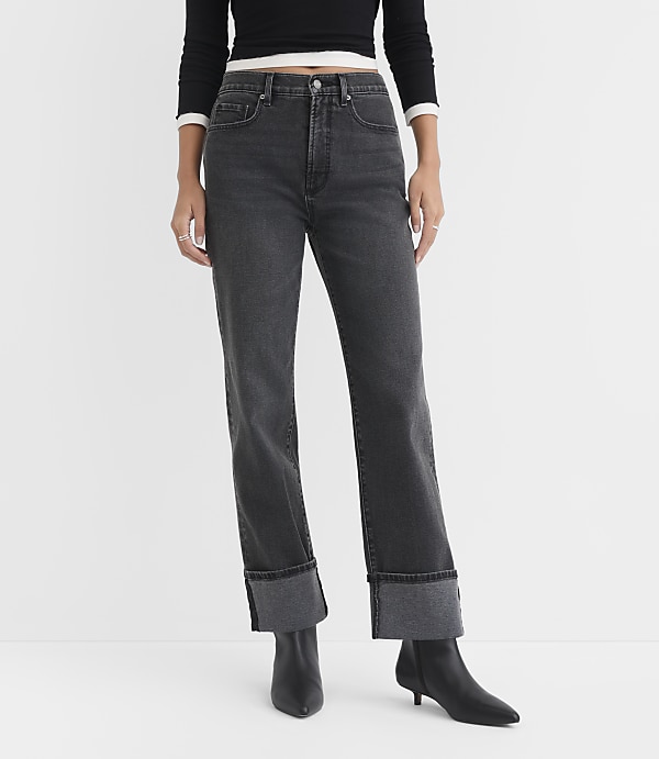 A person stands in the foreground wearing cuffed dark wash jeans and black boots against a plain white background.