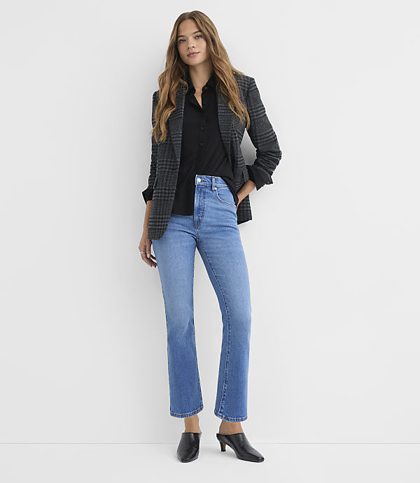 A woman in a black shirt, plaid blazer, and light wash jeans stands against a plain white background.