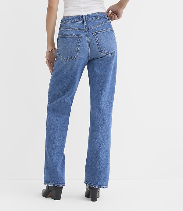 A person wearing blue jeans and black boots stands against a plain white background.